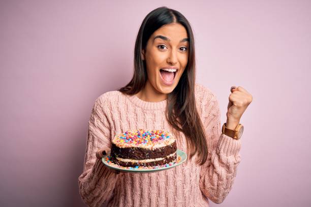 Young beautiful brunette woman holding birthday delicious cake over pink background screaming proud and celebrating victory and success very excited, cheering emotion Young beautiful brunette woman holding birthday delicious cake over pink background screaming proud and celebrating victory and success very excited, cheering emotion woman birthday cake stock pictures, royalty-free photos & images