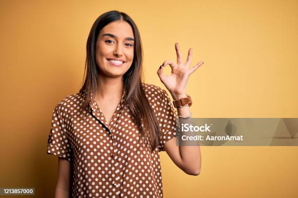 Young Beautiful Brunette Woman Wearing Casual Shirt Over Isolated Yellow Background Smiling Positive Doing Ok Sign With Hand And Fingers Successful Expression Stock Photo - Download Image Now