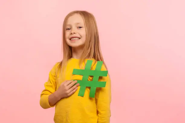 Photo of Children and internet popularity. Portrait of happy beautiful little girl holding hashtag symbol