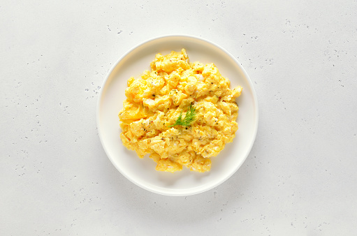 Scrambled eggs on plate over white stone background. Top view, flat lay