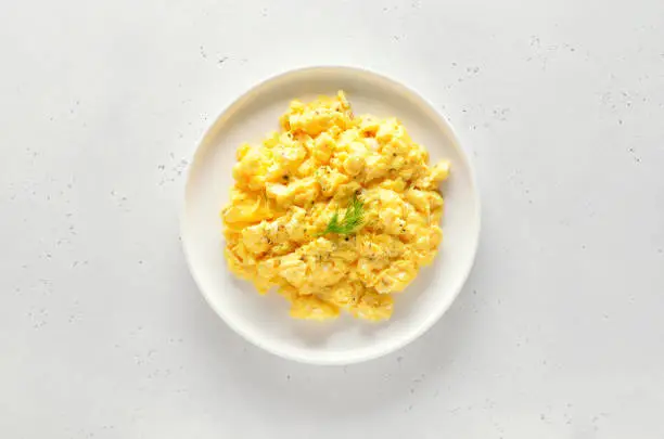 Photo of Scrambled eggs on plate over white stone background