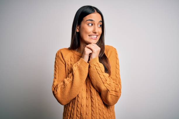 Young beautiful brunette woman wearing casual sweater over isolated white background laughing nervous and excited with hands on chin looking to the side Young beautiful brunette woman wearing casual sweater over isolated white background laughing nervous and excited with hands on chin looking to the side embarrassment stock pictures, royalty-free photos & images