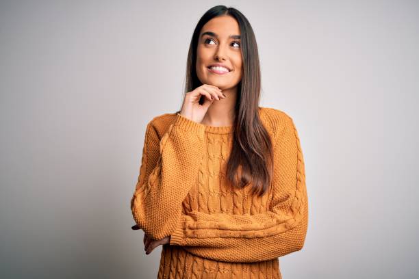 Young beautiful brunette woman wearing casual sweater over isolated white background with hand on chin thinking about question, pensive expression. Smiling and thoughtful face. Doubt concept. Young beautiful brunette woman wearing casual sweater over isolated white background with hand on chin thinking about question, pensive expression. Smiling and thoughtful face. Doubt concept. women beautiful studio shot isolated on white stock pictures, royalty-free photos & images