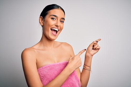 Young beautiful brunette woman wearing towel after shower over isolated white background smiling and looking at the camera pointing with two hands and fingers to the side.