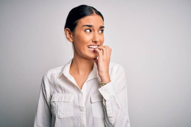 jeune belle femme brune utilisant la chemise occasionnelle au-dessus du fond blanc isolé regardant stressé et nerveux avec des mains sur la bouche mordant des ongles. problème d’anxiété. - bad habit fear emotional stress women photos et images de collection