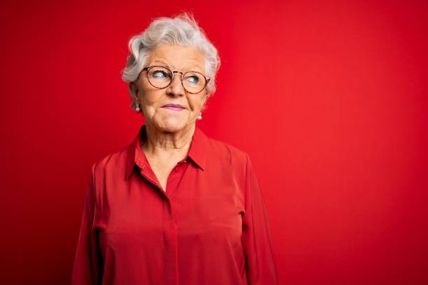 senior beautiful grey-haired woman wearing casual shirt and glasses over red background smiling looking to the side and staring away thinking. - mannered imagens e fotografias de stock