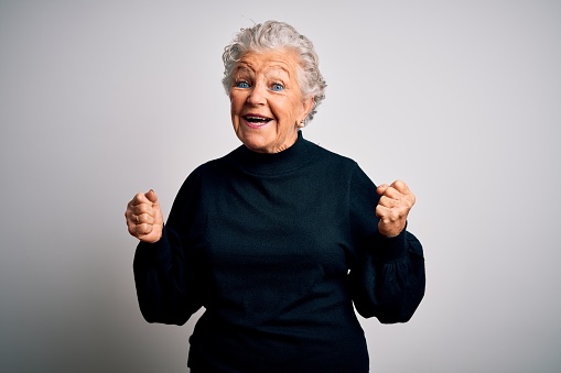 Senior beautiful woman wearing casual black sweater standing over isolated white background celebrating surprised and amazed for success with arms raised and open eyes. Winner concept.