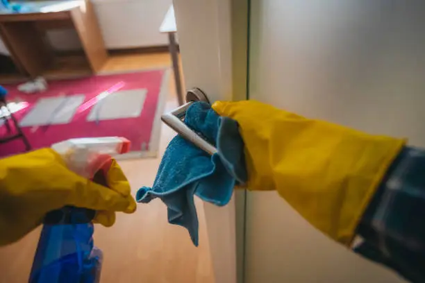 An unknown person cleans the door handle with a disinfectant spray and a magic cloth