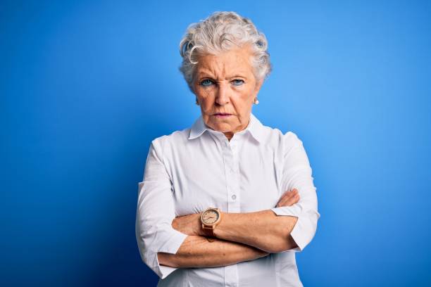 bella donna anziana che indossa una camicia elegante in piedi su uno sfondo blu isolato scettico e nervoso, espressione disapprovante sul viso con le braccia incrociate. persona negativa. - sullen foto e immagini stock