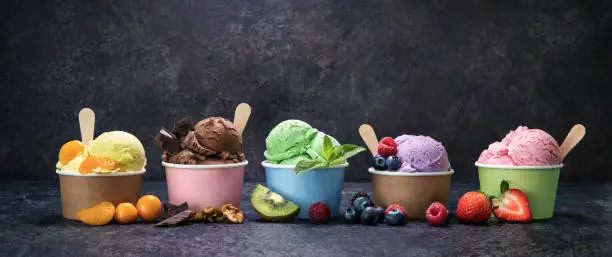 Various colorful ice cream in paper cup on dark rustic background