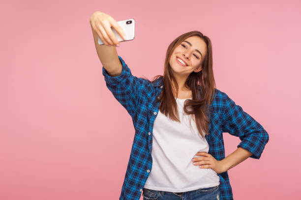 retrato de chica bastante alegre en camisa a cuadros sonriendo y tomando selfie usando el teléfono móvil, - original fotos fotografías e imágenes de stock