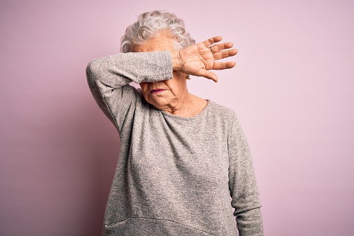 Senior beautiful woman wearing casual t-shirt standing over isolated pink background covering eyes with arm, looking serious and sad. Sightless, hiding and rejection concept
