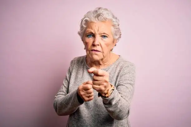 Photo of Senior beautiful woman wearing casual t-shirt standing over isolated pink background Ready to fight with fist defense gesture, angry and upset face, afraid of problem