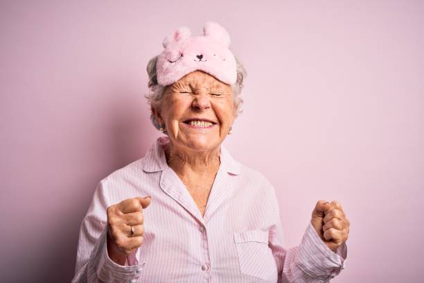 femme belle aînée utilisant le masque de sommeil et le pyjama au-dessus du fond rose isolé excité pour le succès avec les bras levés et les yeux fermés célébrant le sourire de victoire. concept gagnant. - seulement des femmes seniors photos et images de collection