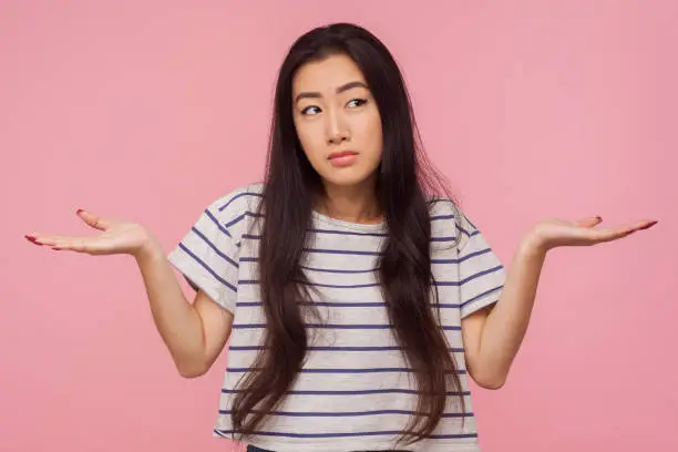 Don't know answer! Portrait of clueless confused girl with long hair in striped t-shirt raising hands in bewilderment, puzzled with question, having doubts. studio shot isolated on pink background