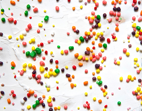 Rainbow colored candy sprinkled on a white background.