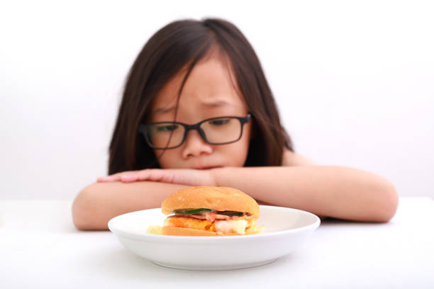 Little Asian girl showing sour face, refusing to eat her food.