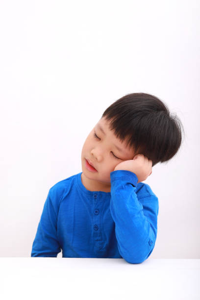 Portrait of tired little asian boy eyes closed and resting on table, isolated on white background.