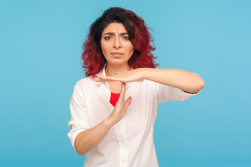 Please, enough for me, need break! Portrait of tired woman with fancy red hair in white shirt showing time out gesture, asking to change deadline, limit. indoor studio shot isolated on blue background