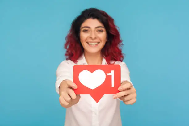 Photo of Portrait of beautiful woman with fancy red hair showing social media heart Like icon, symbol of popularity in internet