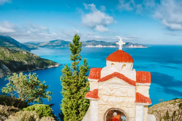 Summer vacation in Greece. Orange colored Hellenic shrine Proskinitari with blue sea and white clouds in background.