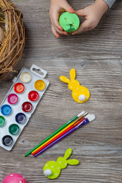 istock baby hand turn easter egg. In wooden table paints, brushes, bunny, nest 1213879870