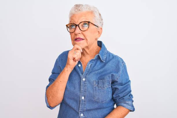 mujer de pelo gris mayor con camisa de mezclilla y gafas sobre fondo blanco aislado con la mano en la barbilla pensando en la pregunta, expresión pensativa. cara sonriente y pensativa. concepto de duda. - portrait senior adult confusion women fotografías e imágenes de stock