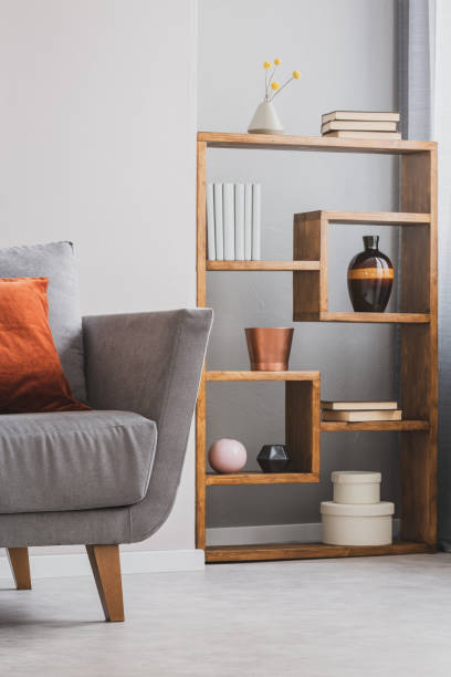 istock Fancy wooden bookshelf with vases and boxes next to grey scandinavian couch 1213885080