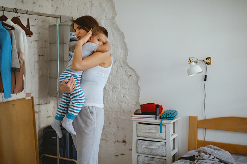 Mother standing in the bedroom and holding toddler in arms for consolation