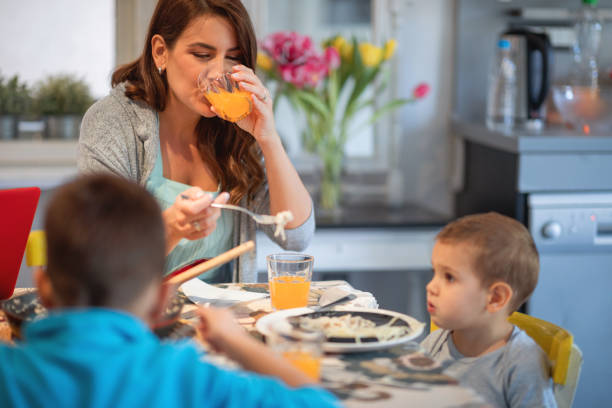 istock Mother drinking juice and feeding toddler spaghetti 1213885706