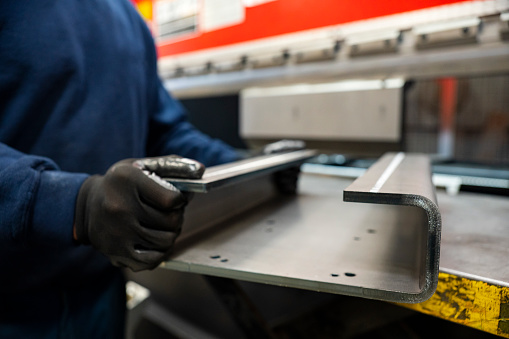 A manufacturing worker holding a formed metal part made by a brake press. Formed metal parts are made using brake presses and laser cutting CNC machines.