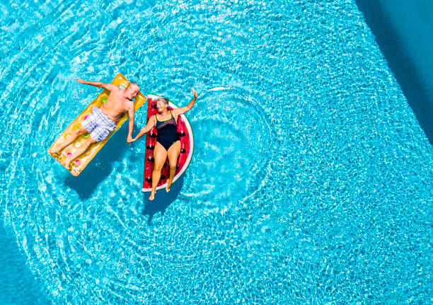 Vertical view of happy couple of old senior people enjoying the summer holiday vacation at the blue water pool with coloured treny lilos together with fun and love Vertical view of happy couple of old senior people enjoying the summer holiday vacation at the blue water pool with coloured treny lilos together with fun and love inflatable photos stock pictures, royalty-free photos & images