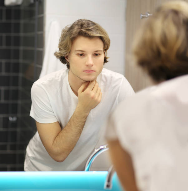 istock young man looking in the mirror,combing his hair,looking at problems on face 1213887079
