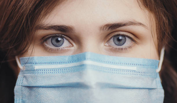 istock sad eyes of serious young woman face in a protective medical mask on colored studio background, girl looking at the camera, concept of health and quarantine measures 1213888607