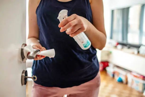 Woman hand spraying alcohol sanitizer bottle to the door handle, against Novel coronavirus or Corona Virus Disease (Covid-19) at public indoor. Antiseptic, Hygiene and Healthcare concept