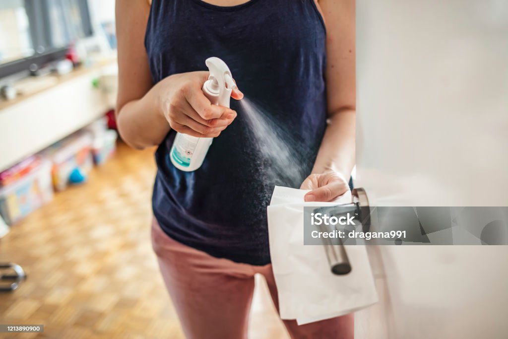 Girl staying at home during coronavirus outbreak Woman cleaning a door handle with a disinfection spray and disposable wipe. Woman sanitizing door handle with antibacterial spray. Girl staying at home during coronavirus outbreak Cleaning Stock Photo