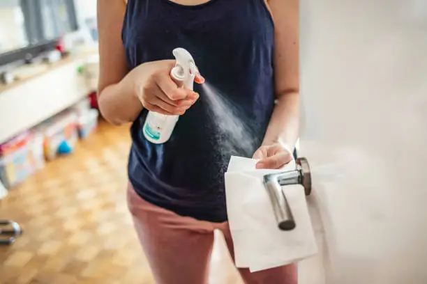 Woman cleaning a door handle with a disinfection spray and disposable wipe. Woman sanitizing door handle with antibacterial spray. Girl staying at home during coronavirus outbreak
