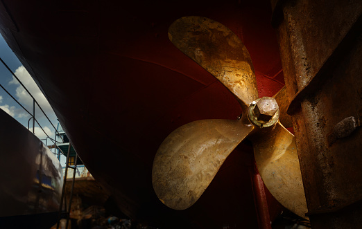 Shallow focus of a newly fitted metal outboard boat propeller attached to s ginseng boat located on a shingle beach.