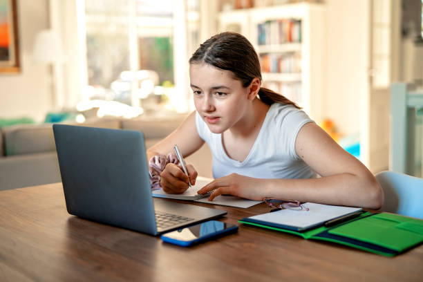 ragazza adolescente che studia online a casa guardando il laptop durante il periodo di isolamento della quarantena durante la pandemia. scuola a casa. distanza sociale. test scolastico online. - home schooling foto e immagini stock