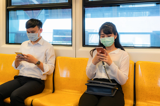 Two Asian people wearing mask sitting in subway distance for one seat from other people keep distance protect from COVID-19 viruses and people social distancing  for infection risk and disease prevention measures.