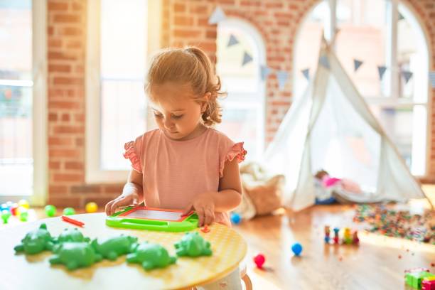 istock Beautiful blond toddler girl drawing using digital board at kindergarten 1213898162