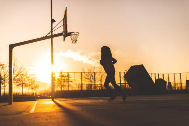 Silhouette of a young woman in motion running on the basketball court at dawn