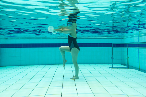 Underwater shot of a woman doing physiotherapy exercises in the water using free-weights