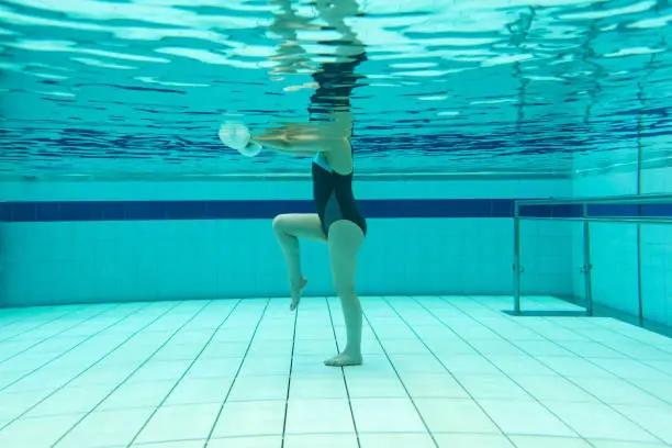 Underwater shot of a woman doing physiotherapy exercises in the water using free-weights