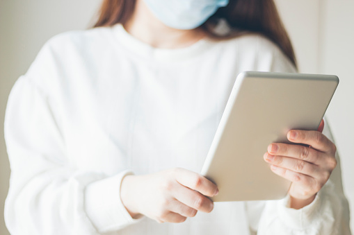 Young woman protected with a medical mask, using a tablet as a means of work and information, COVID-19, coronavirus, selective focus