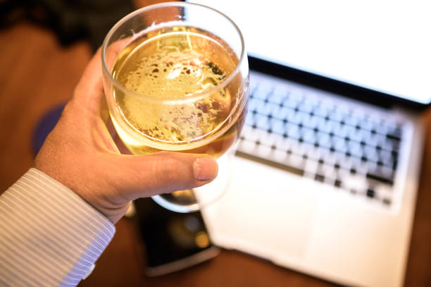 Successful young businessman holding a glass of beer at the end of his working day Successful young businessman holding a glass of beer at the end of his working day. Selective focus. Laptop, smart phone and tie in unfocused background. View from above End of the work day, time to relax. Technology concept friday stock pictures, royalty-free photos & images