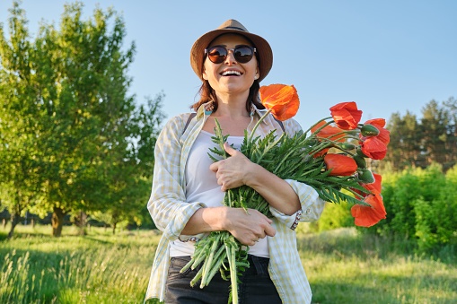 Portrait of beautiful mature healthy happy woman with bouquet of red poppies in countryside