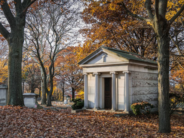 Mausoleum in a cemetery in autumn A mausoleum and several tombstones in a graveyeard surrounded by fall foliage mausoleum photos stock pictures, royalty-free photos & images