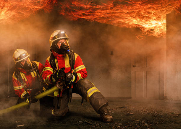 Two firefighters in a burning house The firefighters wear respiratory protection to fight the fire, which protects them from toxic flue gases. Above you develops an ignition of hot smoke, also called flashover. fire station stock pictures, royalty-free photos & images