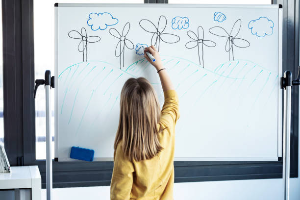 Little girl drawing a eolic park on a whiteboard with a marker pen at home. Shot of little girl drawing a eolic park on a whiteboard with a marker pen at home. kids using smart board stock pictures, royalty-free photos & images